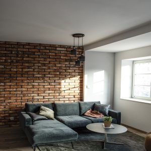 Salon z ceglaną ścianą, narożną sofą i lampą wiszącą
