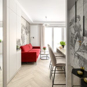 Salon z czerwoną sofą i jasną zabudową do sufitu w mieszkaniu wzorcowym Lokum Porto