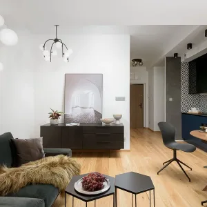 Salon z czarną komodą i jadalnią przy kuchni z granatowymi frontami