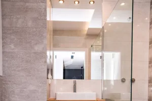 Meble łazienkowe na wymiar – biała szafka podumywalkowa z drewnianym blatem, umywalka nablatowa i kabina prysznicowa bez brodzika – realizacja Litomska, MTW Studio