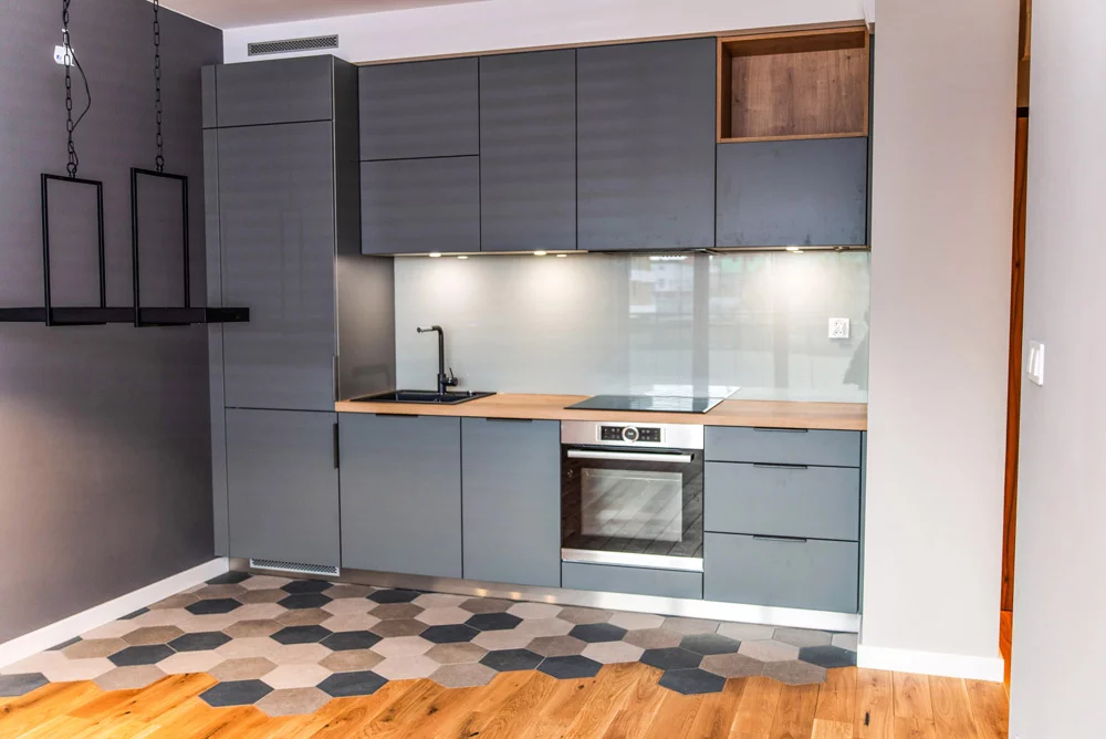 Kuchnia na wymiar z frontami w kolorze antracytu, drewnianym blatem i szklaną ścianą za blatem roboczym – MTW Studio Wrocław